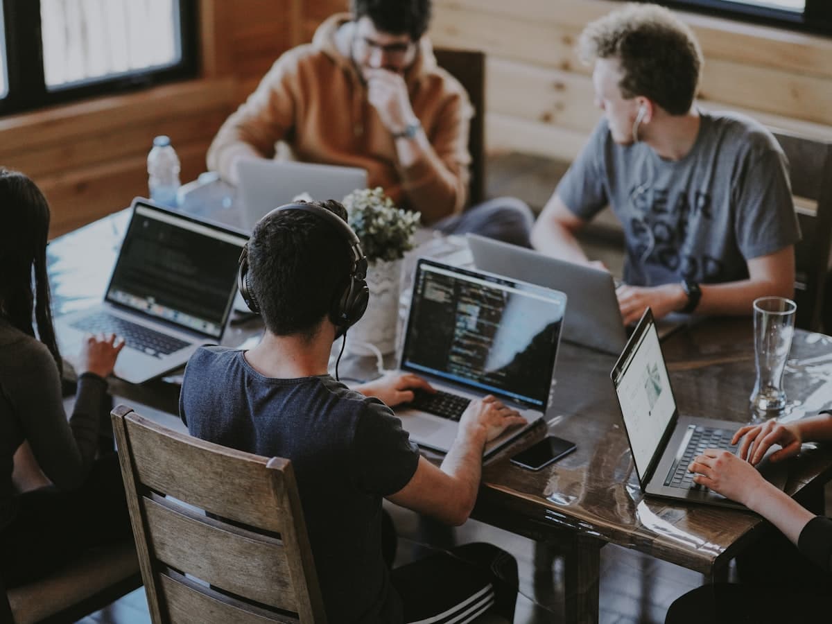 Team Augmentation — developers collaborating at a table with laptops and code on screens